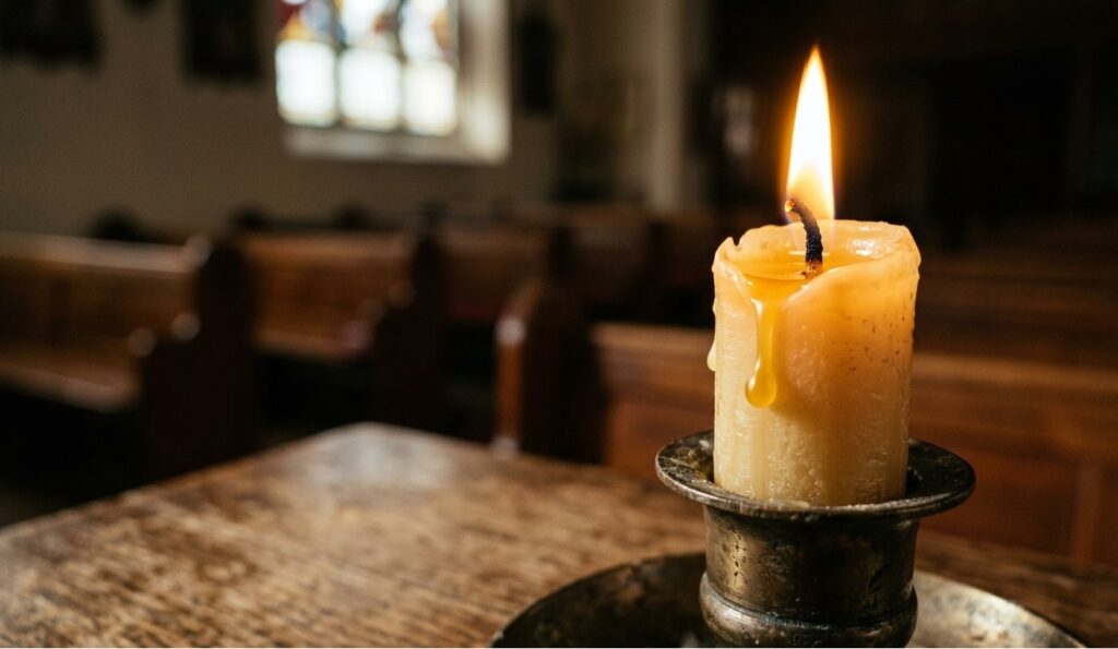 Zbliżenie na płonącą woskową świecę ołtarzową z kapiącą kroplą wosku w surowym wnętrzu kościoła.